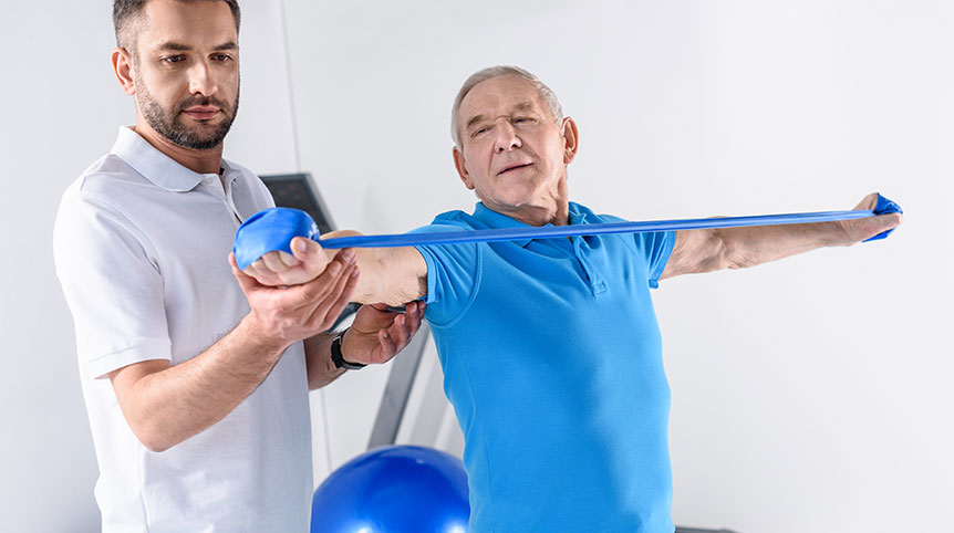 Portrait of rehabilitation therapist assisting senior man exercising with rubber tape.