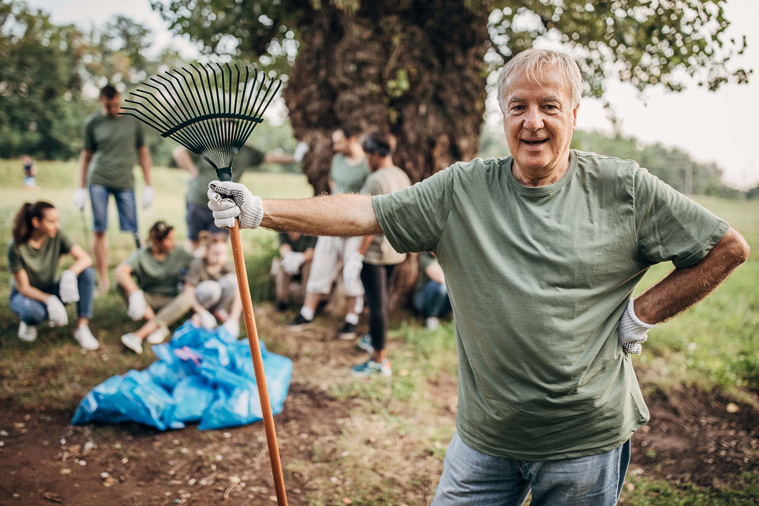 Senior man holding a rake with a group of volunteers standing behind him.