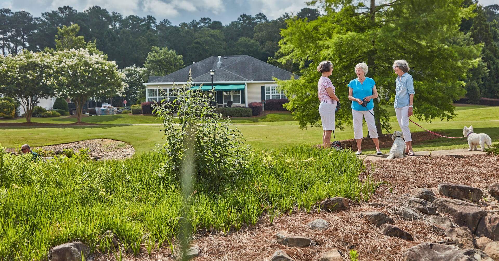 Three women with a dog talking outside along a walking path.