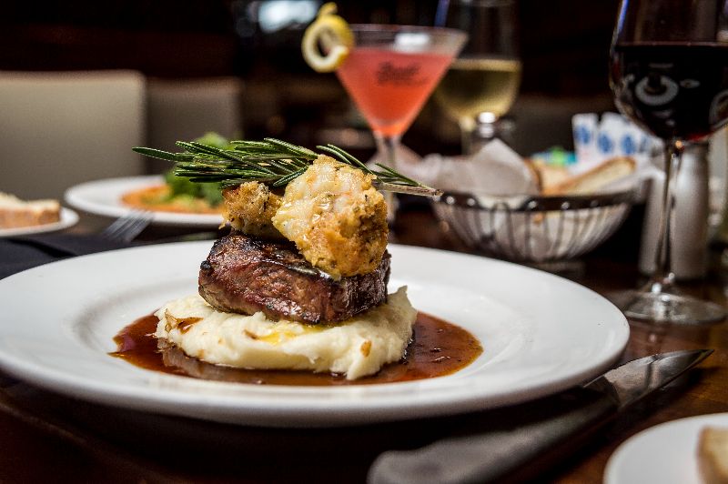 fine dining plate of steak and mashed potatoes, on dining table with glass of wine