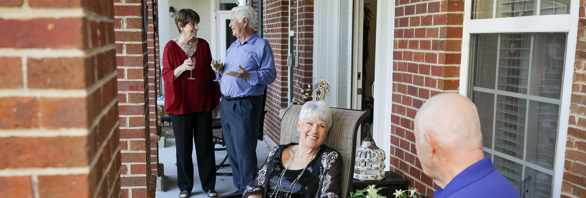 Two older couples on an apartment porch enjoying a drink and conversations.