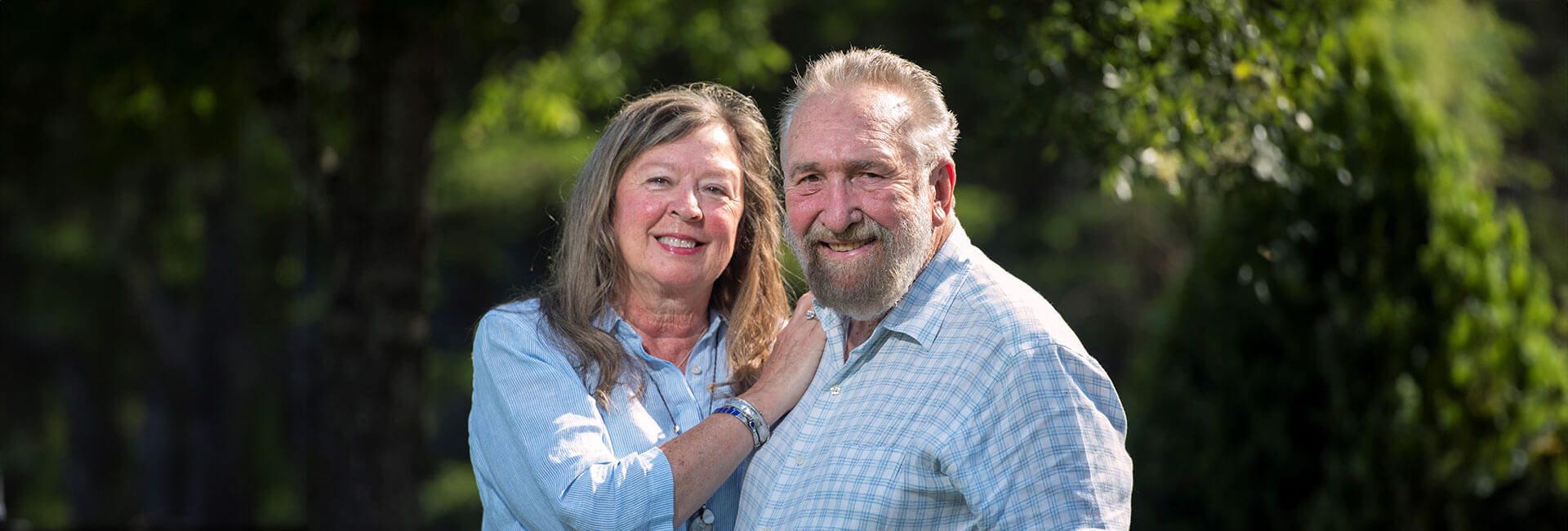 Senior couple in light blue shirts posing outside for a picture.